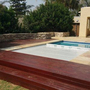 designer pool covers A wooden deck with a pool and pool covers in the background.