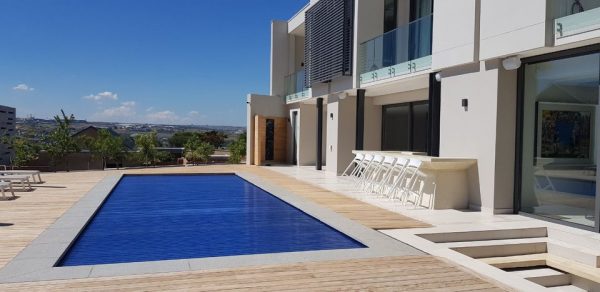 designer pool covers A modern house with a swimming pool and deck featuring pool covers for added safety.