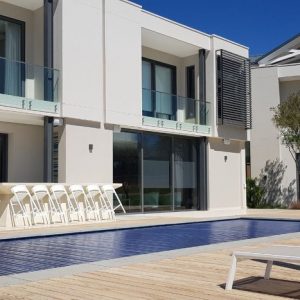 designer pool covers A modern house with a PoolDeck Slatted Automatic Cover 3.5M X 8M and lounge chairs.