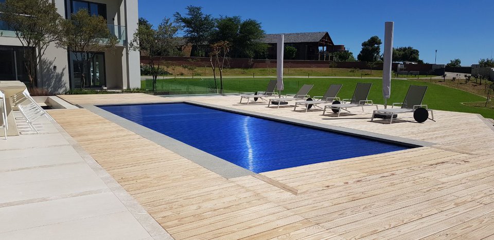 designer pool covers A wooden deck with a swimming pool and lounge chairs featuring pool covers.