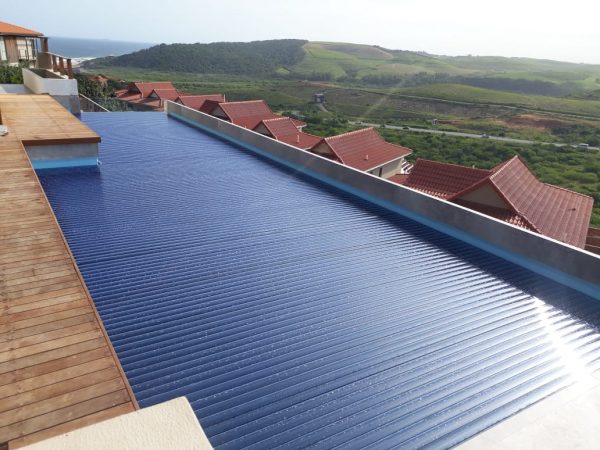 designer pool covers A PoolDeck Slatted Automatic Cover (2500 x 250mm) on a wooden deck with a view of the ocean.