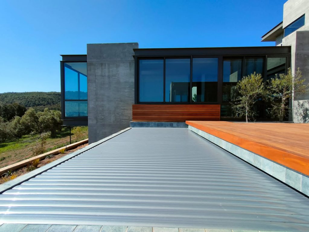 designer pool covers A modern house with a wooden deck, a metal roof, and a swimming pool.