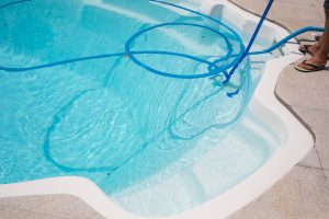 designer pool covers A person managing pool water levels by cleaning a pool with a hose.